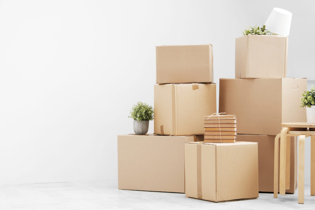 Self-Storage for Students in South Africa: Affordable Solutions for University Breaks 5 Moving boxes stacked on top of each other. Moving to a new home. Belongings in cardboard boxes, books and green plants in pots stand on the gray floor against the background of a white wall. Concept relocation.