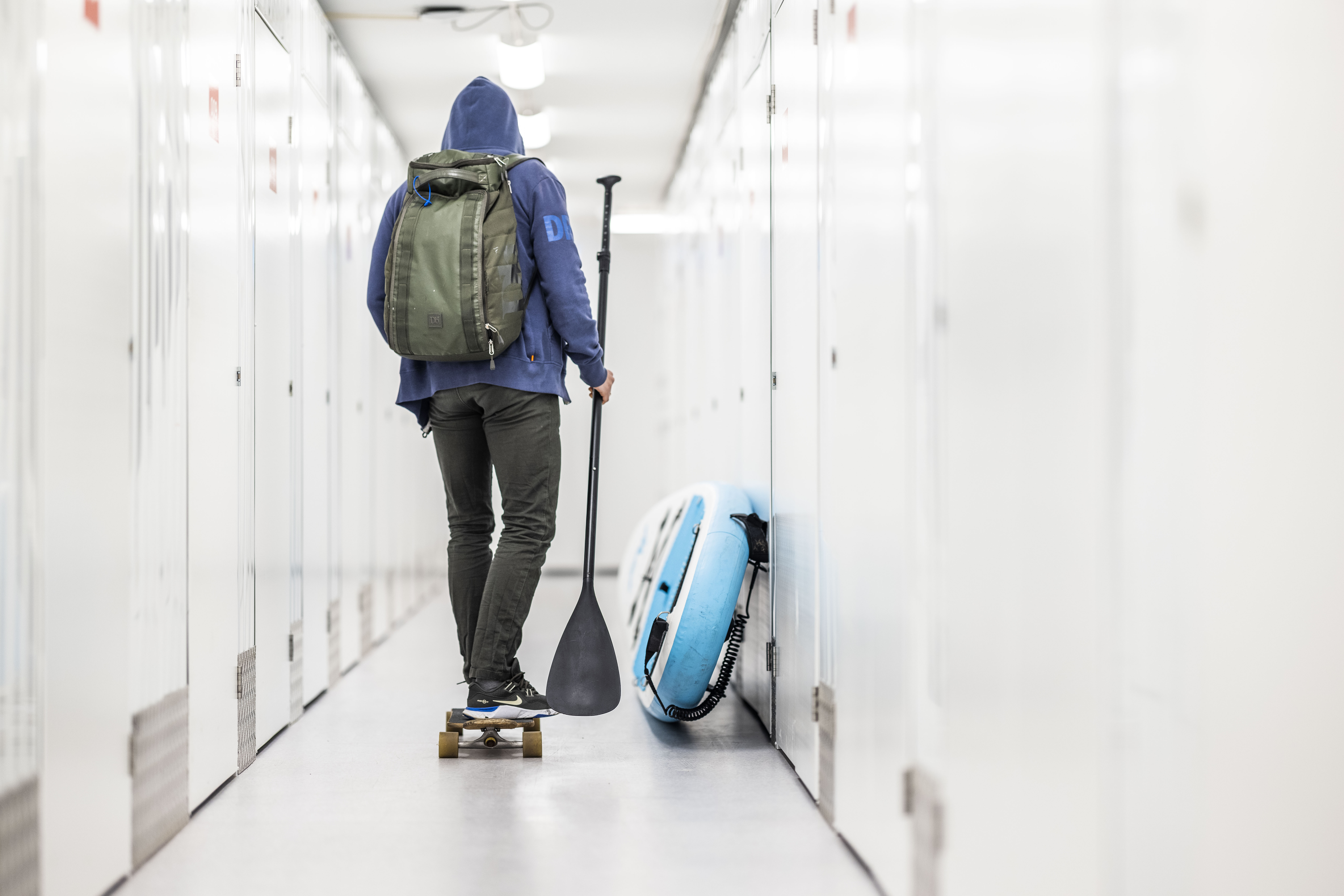 Self-Storage for Students in South Africa: Affordable Solutions for University Breaks 1 Person on a skateboard with a paddle and a backpack in a brightly lit flexistore self-storage facility, next to an inflatable paddleboard.